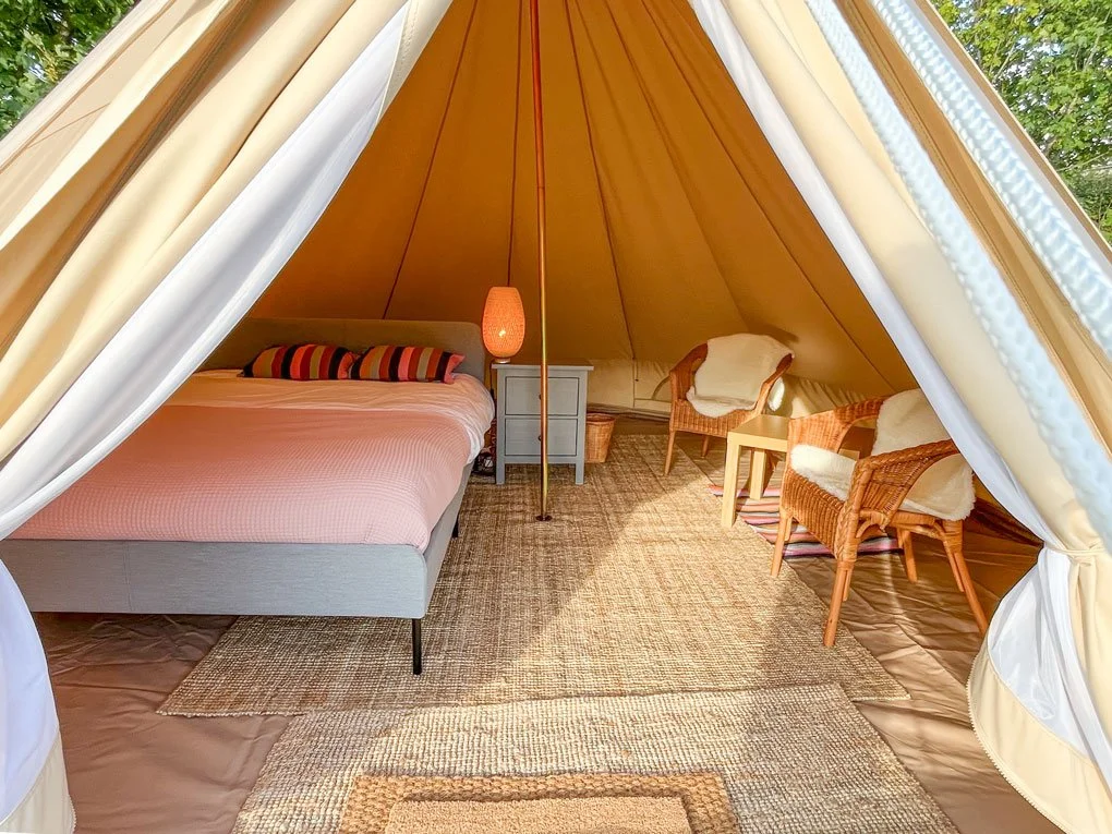 Inside a Greystones Glamping bell tent, with a made-up double bed, warm lighting, rugs and wicker armchairs